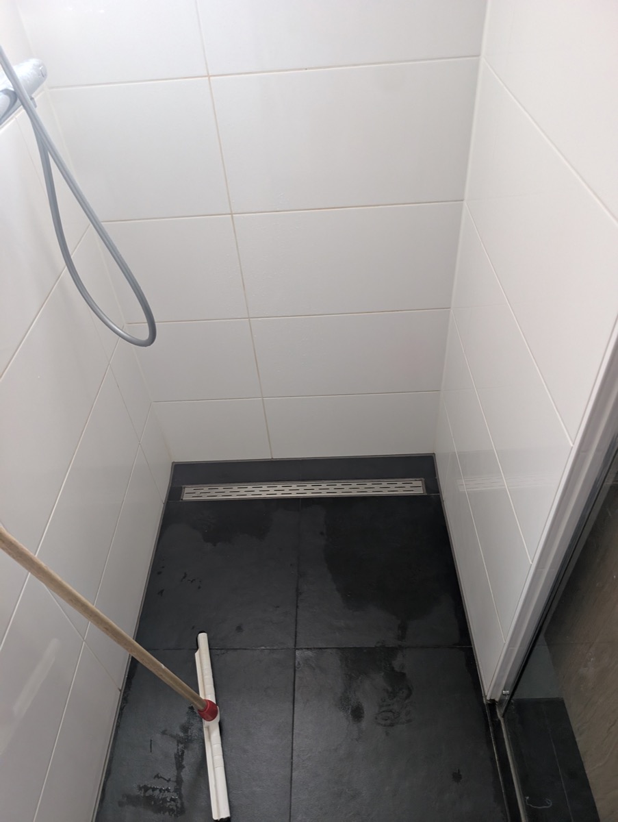 The shower floor, photographed from above, with the linear drain against the far wall.